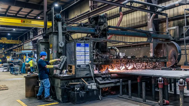 A worker at industrial machinery with sparks flying